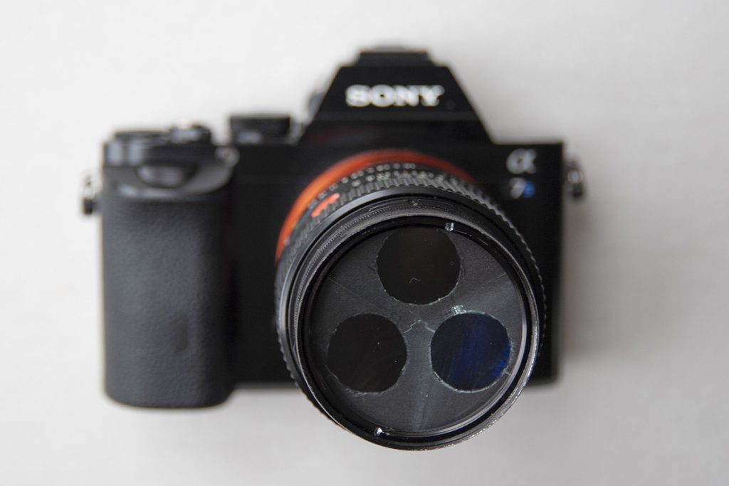 Fig. 4 : Le prisme RGB devant un vieil objectif Canon FD 1:1.4 / 50mm sur un Sony a7S. Attention : La pupille d'entrée effective par canal de couleur est réduite au diamètre du panneau de carton. Les 3 trous ronds ne doivent pas dépasser le diamètre libre de la lentille frontale. L'objectif devra être complétement ouvert.